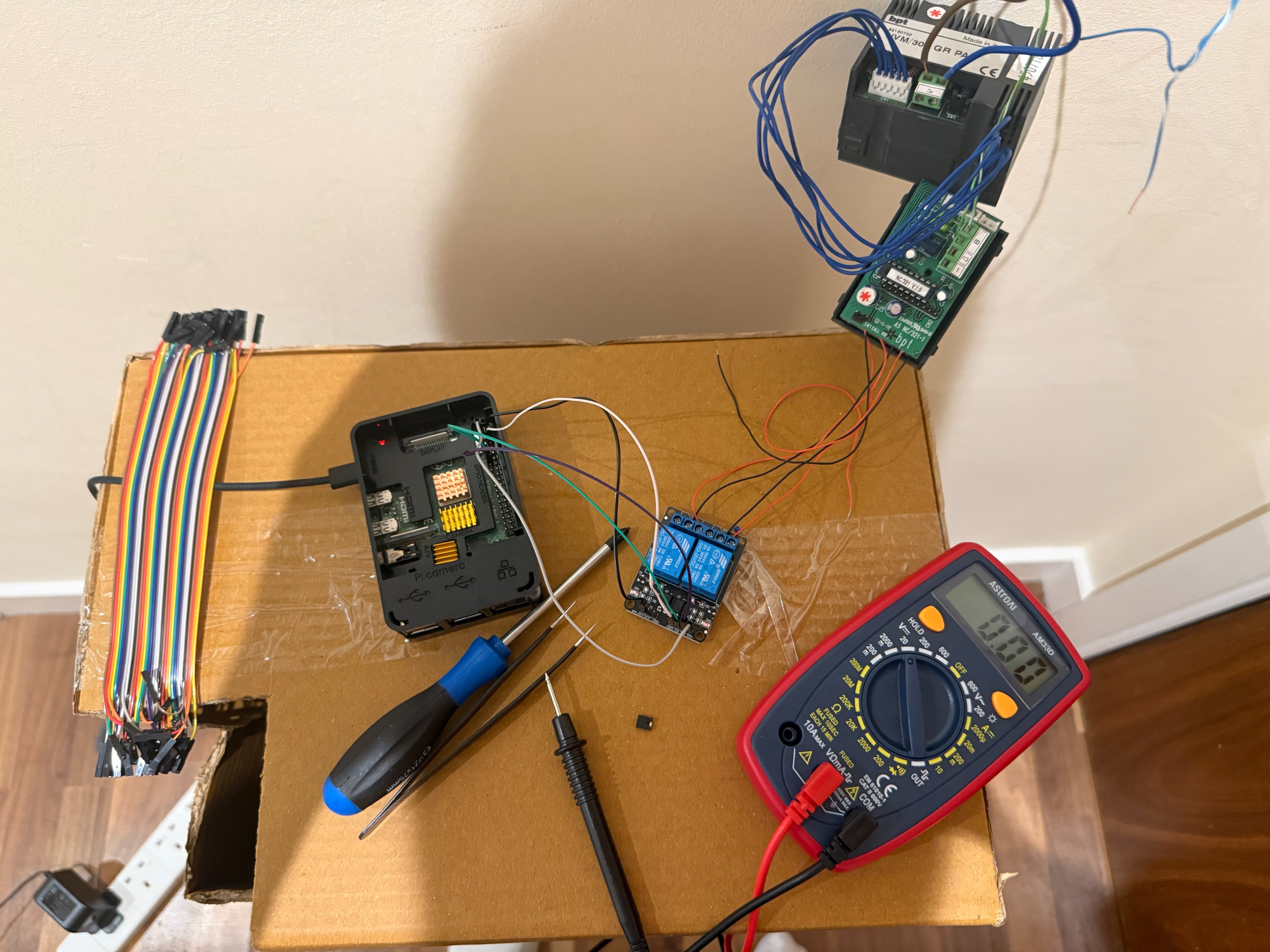 Raspberry Pi, relay board, wires, and multimeter arranged on a cardboard box